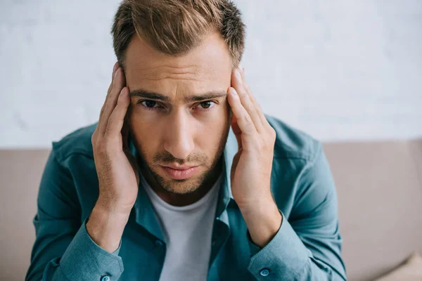 Junger Mann mit Kopfschmerzen blickt zu Hause in die Kamera — Stockfoto