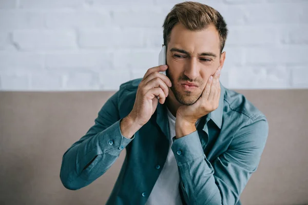 Young man talking by smartphone and suffering from jaw pain at home — Stock Photo