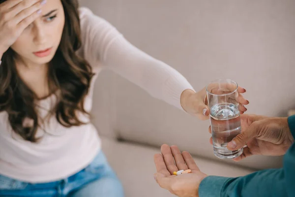 Plan recadré de l'homme donnant un verre d'eau et des pilules à la femme souffrant de maux de tête — Photo de stock