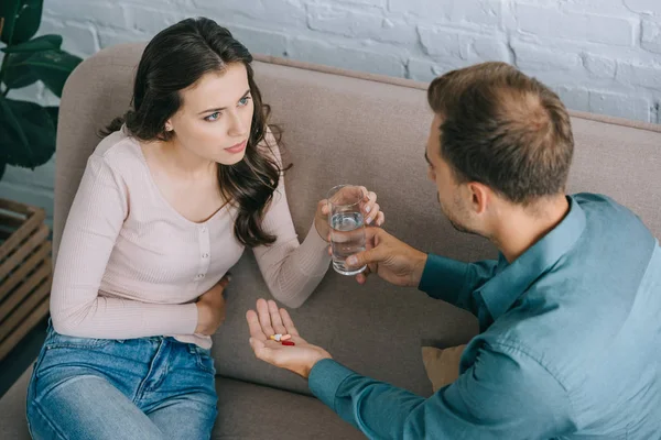 High angle view of man giving glass of water and pills to woman with stomach pain — Stock Photo