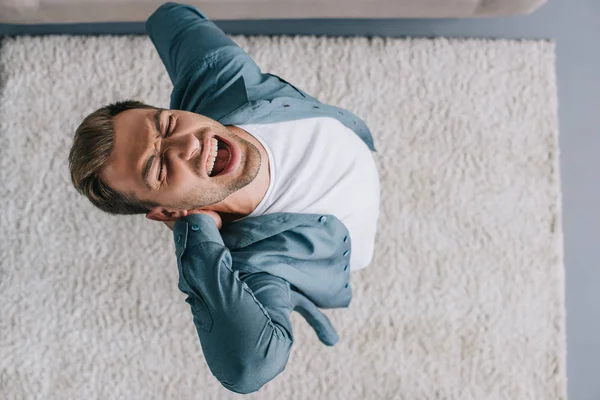 Overhead view of young man screaming and suffering from pain in neck and back at home — Stock Photo