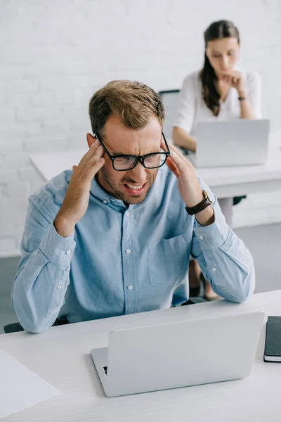 Vista de ángulo alto del hombre de negocios en gafas que sufren de dolor de cabeza mientras trabaja con el ordenador portátil en la oficina - foto de stock