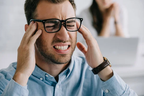 Close-up view of young businessman in eyeglasses suffering from headache in office — Stock Photo