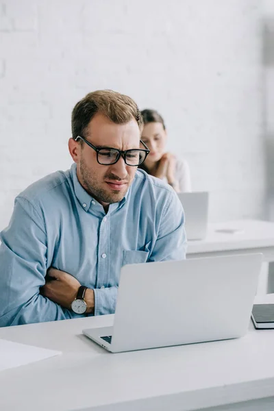 Uomo d'affari con gli occhiali che soffre di dolore mentre lavora con il computer portatile in ufficio — Foto stock