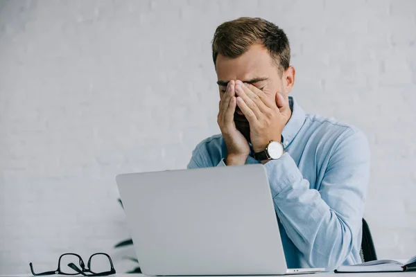 Joven hombre de negocios que sufre de dolor en los ojos mientras trabaja con el ordenador portátil - foto de stock