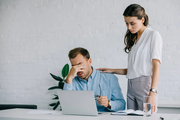 Mujer joven mirando a un colega masculino que sufre de dolor de cabeza en el lugar de trabajo - foto de stock