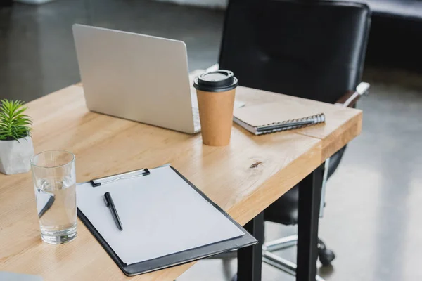 Laptop, área de transferência, vidro de água e café para ir em mesa de madeira no escritório — Fotografia de Stock