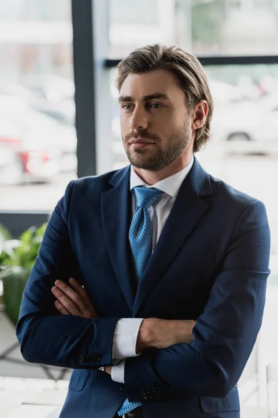 Handsome young bearded businessman in suit standing with crossed arms and looking away — Stock Photo