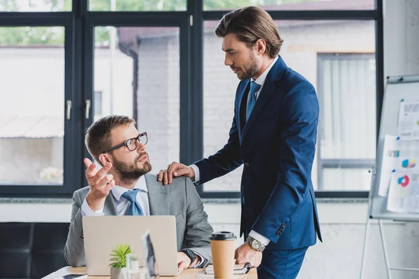 Jóvenes empresarios serios mirándose unos a otros y discutiendo el proyecto en la oficina - foto de stock