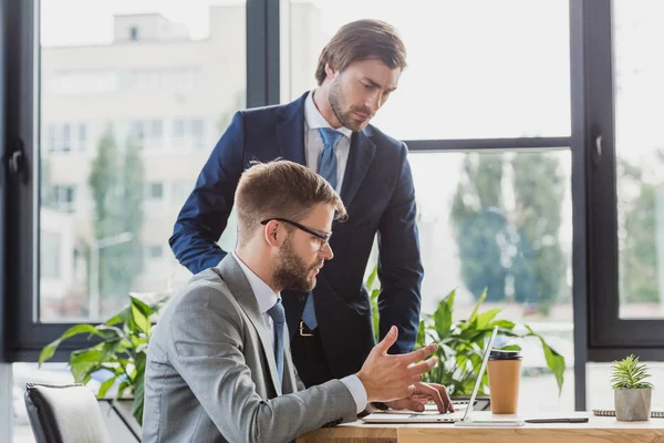 Jóvenes empresarios enfocados utilizando el ordenador portátil mientras trabajan juntos en la oficina - foto de stock