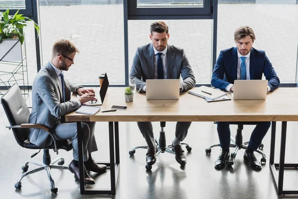 Vista de ángulo alto de los jóvenes empresarios enfocados que utilizan computadoras portátiles en el lugar de trabajo - foto de stock