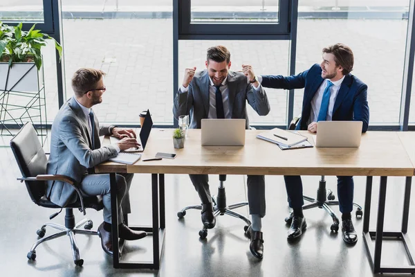 Vista de ángulo alto de jóvenes empresarios felices que trabajan con computadoras portátiles en la oficina - foto de stock