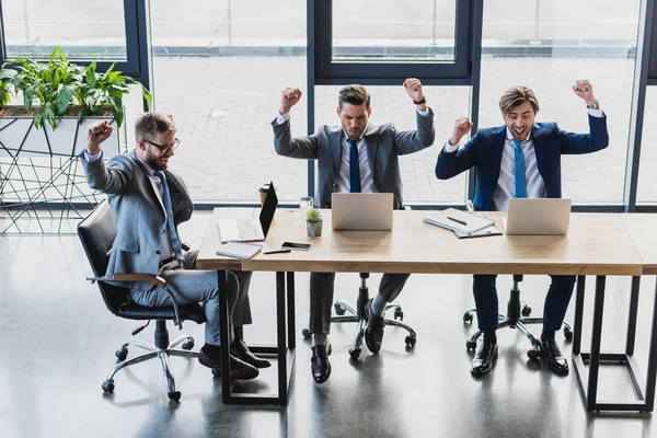 High angle view of triumphing young businessmen working with laptops in office — Stock Photo