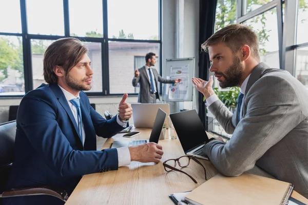 Seitenansicht von jungen Geschäftsleuten, die Laptops benutzen und über Projekte im Büro diskutieren — Stockfoto