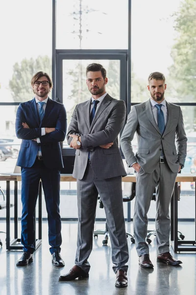 Selbstbewusste junge Geschäftsleute in formaler Kleidung stehen zusammen und blicken im Büro in die Kamera — Stockfoto