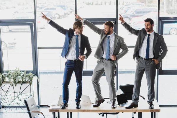 Drei glückliche junge Geschäftsleute tanzen auf Tisch im Büro — Stockfoto