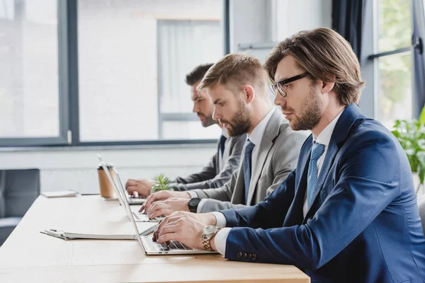 Vue latérale de jeunes hommes d'affaires utilisant des ordinateurs portables dans le bureau — Photo de stock