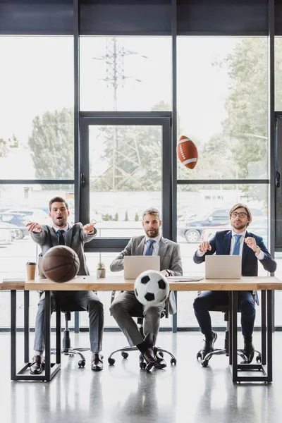 Junge Büroangestellte in formeller Kleidung werfen Bälle, während sie im Büro mit Laptops arbeiten — Stockfoto