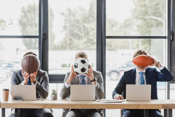 Jóvenes trabajadores de oficina sosteniendo pelotas mientras trabajan con computadoras portátiles en la oficina - foto de stock