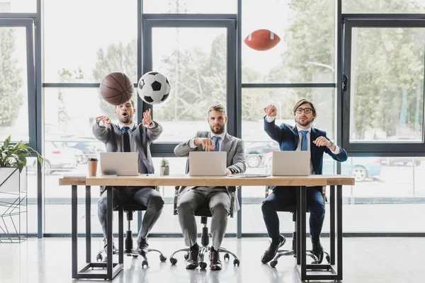 Молодые офисные работники бросают мячи во время работы с ноутбуками в офисе — стоковое фото