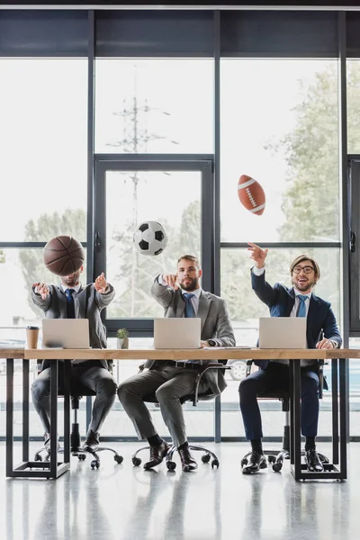 Giovani uomini d'affari che lanciano palle mentre lavorano con i computer portatili in ufficio — Foto stock