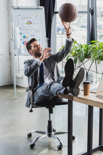 Happy young businessman in suit playing with basketball ball while working on office — Stock Photo