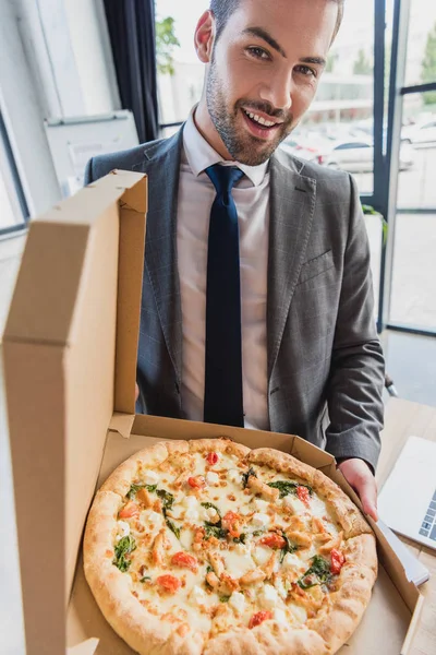 Beau jeune homme d'affaires tenant pizza et souriant à la caméra — Stock Photo