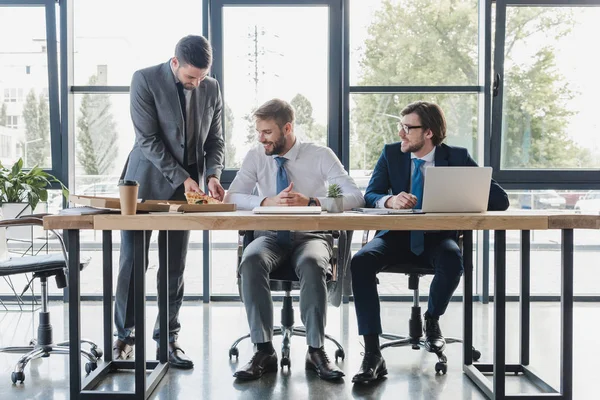 Heureux jeunes employés de bureau en tenue formelle manger de la pizza sur le lieu de travail — Photo de stock