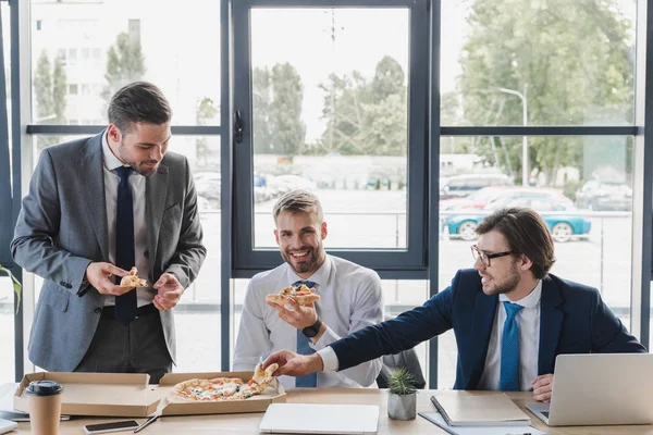 Glückliche junge Büroangestellte, die am Arbeitsplatz Pizza essen — Stockfoto