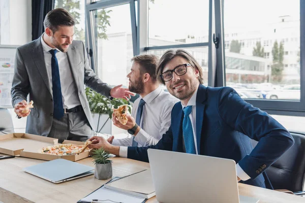 Jóvenes empresarios sonrientes comiendo pizza en el lugar de trabajo - foto de stock