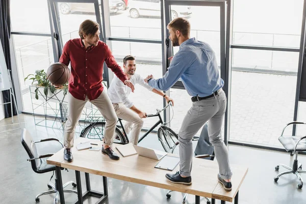 Visão de alto ângulo de jovens empresários se divertindo com bola de basquete no escritório — Fotografia de Stock