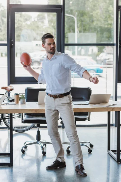 Красивий молодий бізнесмен грає з м'ячем регбі в офісі — стокове фото