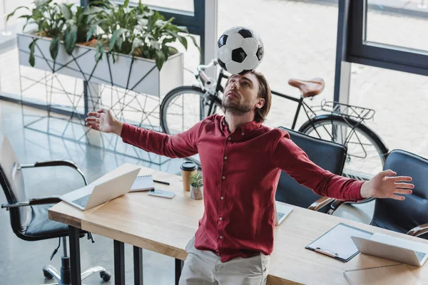 Blick aus der Vogelperspektive auf jungen Geschäftsmann, der im Büro Fußball auf Kopf balanciert — Stockfoto