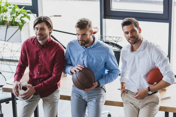 High angle view of young businessmen holding basketball, soccer and rugby balls in office — Stock Photo
