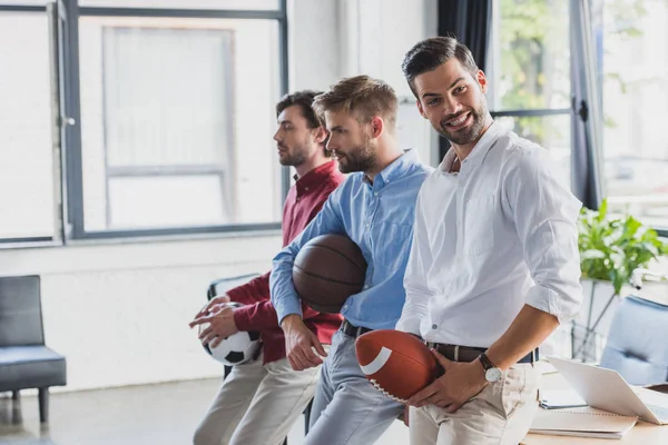 Jóvenes empresarios felices sosteniendo pelotas y mirando hacia otro lado en la oficina - foto de stock