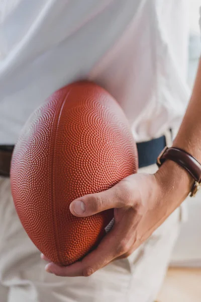 Primer plano vista parcial de hombre de negocios sosteniendo pelota de rugby en la oficina - foto de stock