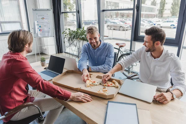 Glückliche junge Geschäftsleute, die am Arbeitsplatz Pizza essen — Stockfoto