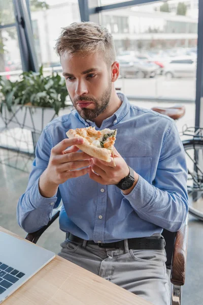 Joven empresario guapo comiendo pizza en la oficina - foto de stock