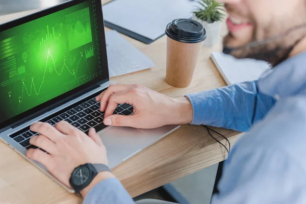 Selektiver Fokus eines lächelnden Geschäftsmannes im Headset mittels Laptop mit Geschäftsdiagrammen auf dem Bildschirm — Stockfoto