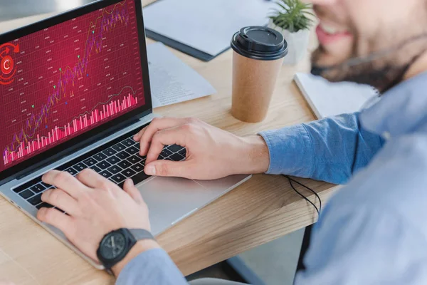 Tiro recortado de empresário sorridente em fone de ouvido usando laptop com gráficos de negócios na tela — Fotografia de Stock