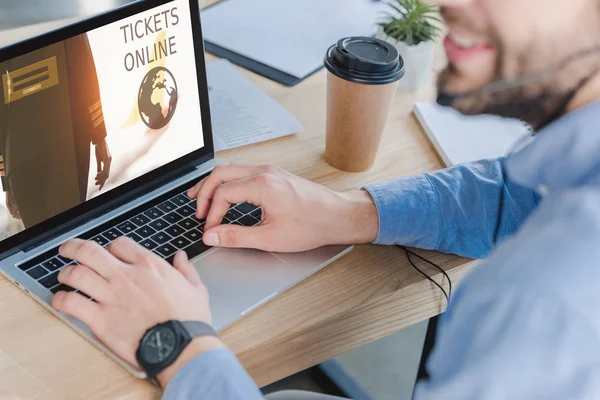 Prise de vue recadrée de l'opérateur de centre d'appels souriant dans un casque à l'aide d'un ordinateur portable avec des billets site Web en ligne à l'écran — Photo de stock