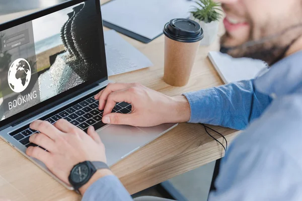 Enfoque selectivo del operador del centro de llamadas sonriente en auriculares utilizando el ordenador portátil con el sitio web de reserva en la pantalla - foto de stock