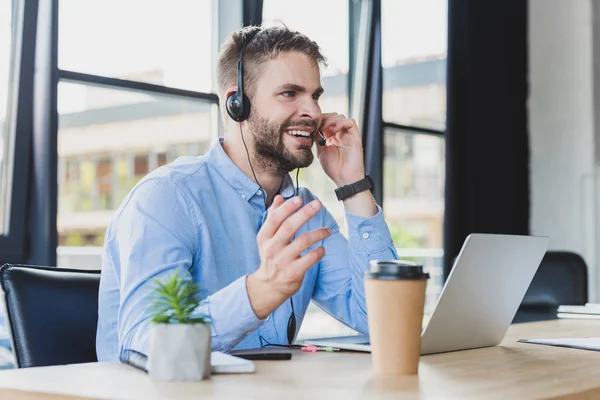 Sorridente giovane operatore di call center in auricolare che lavora con laptop in ufficio — Foto stock