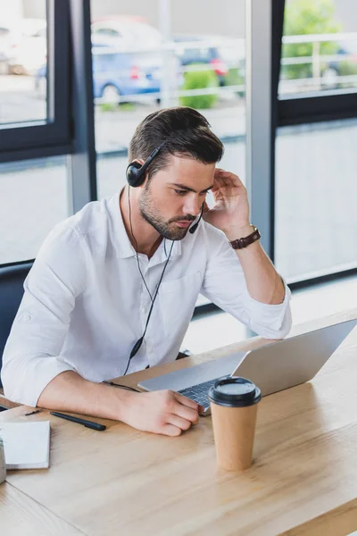 Visão de alto ângulo do operador de call center jovem no fone de ouvido usando laptop no escritório — Fotografia de Stock
