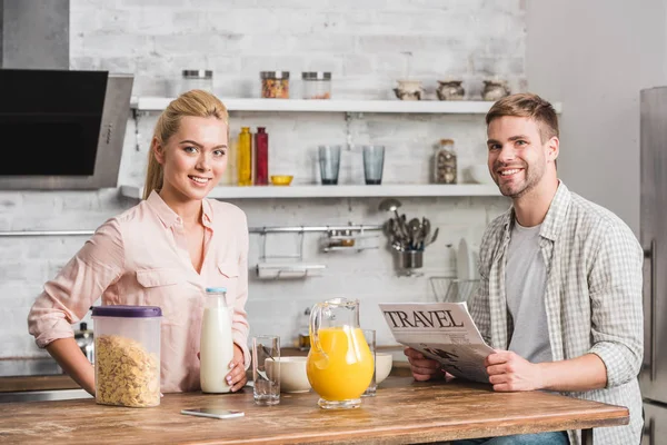 Boyfriend holding travel newspaper and looking at camera in kitchen — Stock Photo