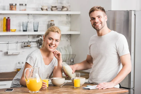 Feliz pareja mirando a la cámara y desayunando en la cocina - foto de stock