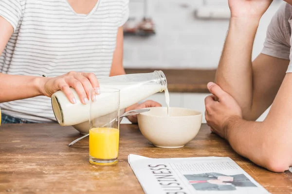 Cropped image of girlfriend pouring milk from bottle into plate with cornflakes during breakfast in kitchen — Stock Photo