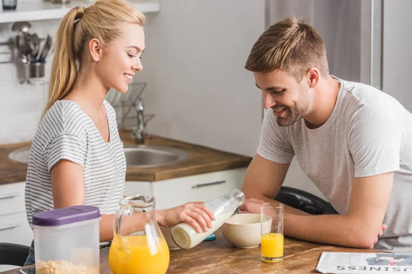 Подружка наливает молоко из бутылки в тарелку парня с кукурузными хлопьями на кухне — стоковое фото