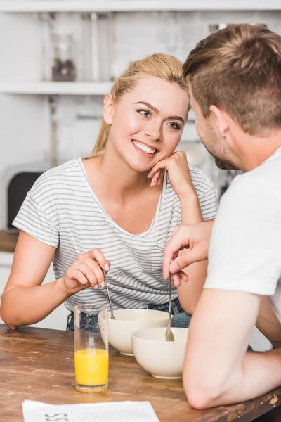 Стомлена усміхнена дівчина дивиться на хлопця під час сніданку на кухні — стокове фото