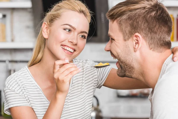Porträt einer lächelnden Freundin, die ihren Freund in der Küche mit Cornflakes füttert — Stockfoto